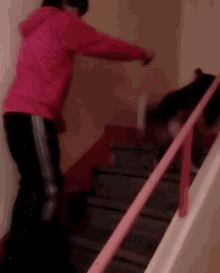 a woman in a pink hoodie is walking down a set of stairs with a pink railing .