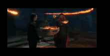 a man is standing in front of a fire while holding a box of pizza .