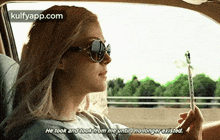 a woman is sitting in the back seat of a car holding a pen and smoking a cigarette .