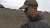a man wearing a baseball cap and a hoodie is standing in a field .