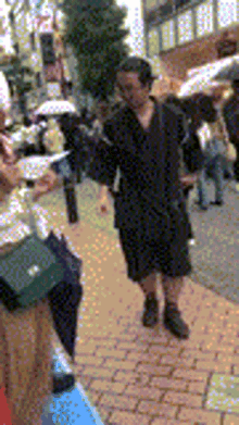 a woman in a black dress is walking down a brick sidewalk holding an umbrella