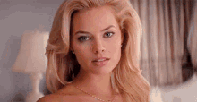 a beautiful blonde woman is wearing a necklace and earrings and looking at the camera .
