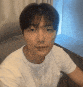a man in a white t-shirt is sitting on a couch and looking at the camera .