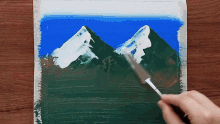 a person is painting a picture of a mountain with a brush