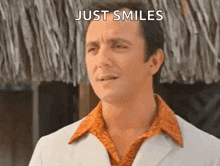 a man in a white suit and orange shirt is smiling and making a funny face .