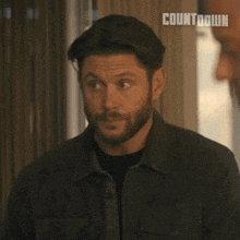 a man with a beard says " please continue " in front of a window