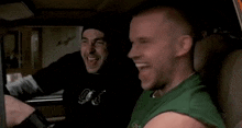 a man in a green shirt is sitting in the back seat of a car laughing and holding a roll of money .