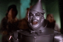 the tin man from the wizard of oz is making a funny face while standing in front of a crowd .