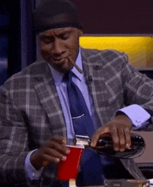 a man in a suit and tie is smoking a cigar while pouring a drink into a red cup .