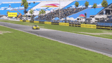 a yellow car is driving down a race track in front of a large stadium