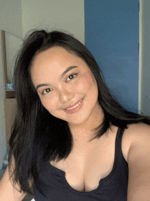 a woman in a black tank top smiles in front of a blue wall