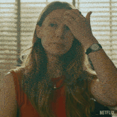 a woman wearing a watch and a red shirt is scratching her forehead