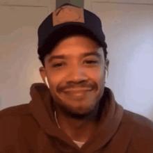 a man wearing a hat and a hoodie is smiling .