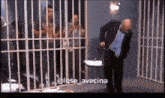 a man in a suit and tie is standing in a jail cell with other people .