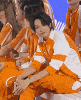 a group of people are sitting on a bench and one of them is wearing orange