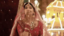 a bride in a red and gold dress is blowing a kiss with her hands .