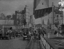 a black and white photo of a group of people riding bikes down a street in front of a destroyed building .
