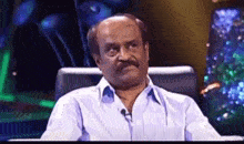 a man with a mustache is sitting in a chair with a microphone in front of him .