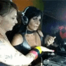 two women wearing headphones are sitting at a table with a computer .