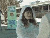 a girl stands in front of a sign that says " stop the spread of covid 19 we are this together "