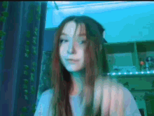 a girl with long brown hair and blue eyes is sitting in front of a blue wall .