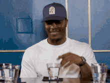 a man wearing a white shirt and a blue hat is sitting at a table with glasses of water
