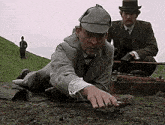 a man in a suit and hat is crawling on the ground next to another man .