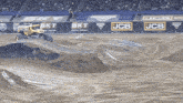 a monster truck is on a dirt track with a jcb banner in the background