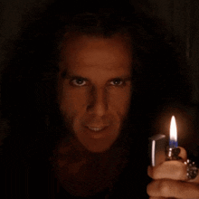 a man with long hair is holding a lighter in his hand and smiling .