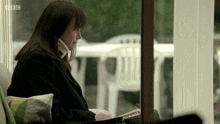a woman sits in front of a window with bbc written on the bottom left