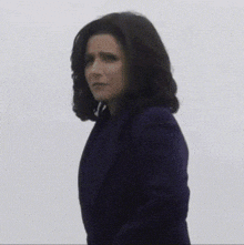 a woman in a blue coat is standing in front of a white wall