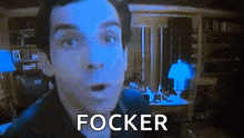 a man is standing in a dark room with his mouth open and the word focker written on the screen behind him .