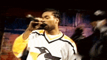 a man singing into a microphone wearing a yellow and white jersey with a bird on it