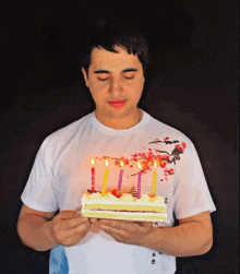 a man in a white shirt is holding a birthday cake with lit candles