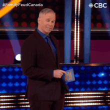 a man in a suit and tie is standing in front of a podium with the words family feud canada behind him