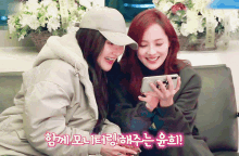 two women sitting on a couch looking at a cell phone with chinese writing on the bottom right