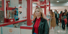 a woman in a red shirt and black leather jacket is walking in a netflix ad