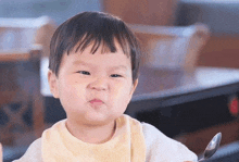 a baby is sitting at a table with a spoon in his mouth and making a face .