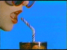 a woman wearing sunglasses is drinking through a straw from a glass