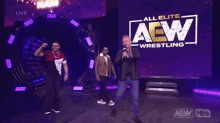 a man with a microphone stands in front of a sign that says aew