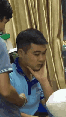a man in a blue shirt has a hand on his chin while another man looks on