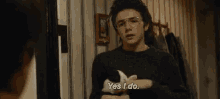 a young man wearing glasses and a black sweater is holding a napkin and saying `` yes i do '' .