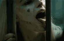 a woman with a tattoo on her face is sticking her tongue out behind a fence .