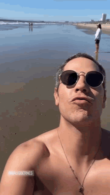 a shirtless man wearing sunglasses takes a selfie on a beach