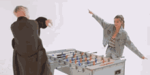 a man in a robe and a woman in a denim jacket are playing foosball