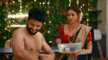a man without a shirt is standing next to a woman holding a container .