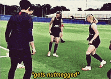 a group of soccer players are playing on a field and one of them says " gets nutmegged "