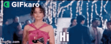 a woman in a pink dress is standing in front of a crowd and says hi