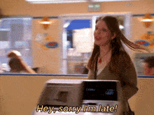 a woman standing in front of a machine that says sorry i 'm late