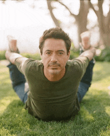 a man in a green shirt is doing yoga on the grass .